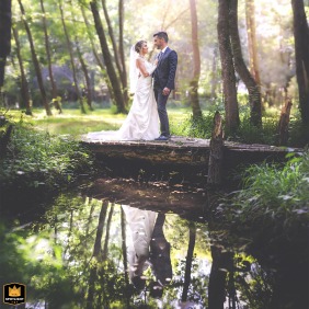   On the lush banks of the Caudeau River in Liorac/Louyre, Dordogne, the couple poses together, with tranquil water and natural greenery creating a peaceful, romantic setting.
